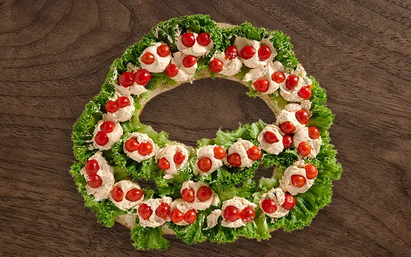 Riesen-Brezel von oben, offen: auf Salatblättern liegen Rosetten aus Frischkäse, auf jeder eine halbe Kirschtomate.