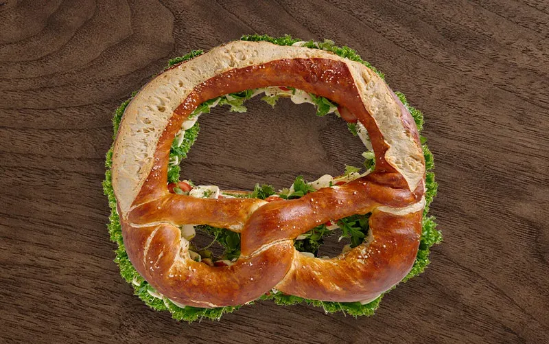 Riesen-Brezel von oben, geschlossen: der Laugenteig liegt über der Füllung, an den Rändern schauen Käse und Salat heraus.