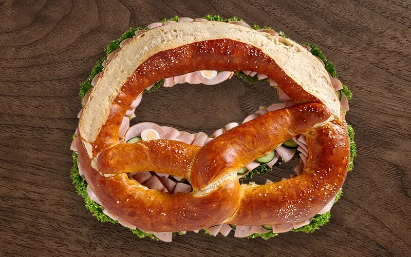 Riesen-Brezel von oben, geschlossen: der Laugenteig liegt über der Füllung, an den Rändern schauen Schinken und Salat heraus.