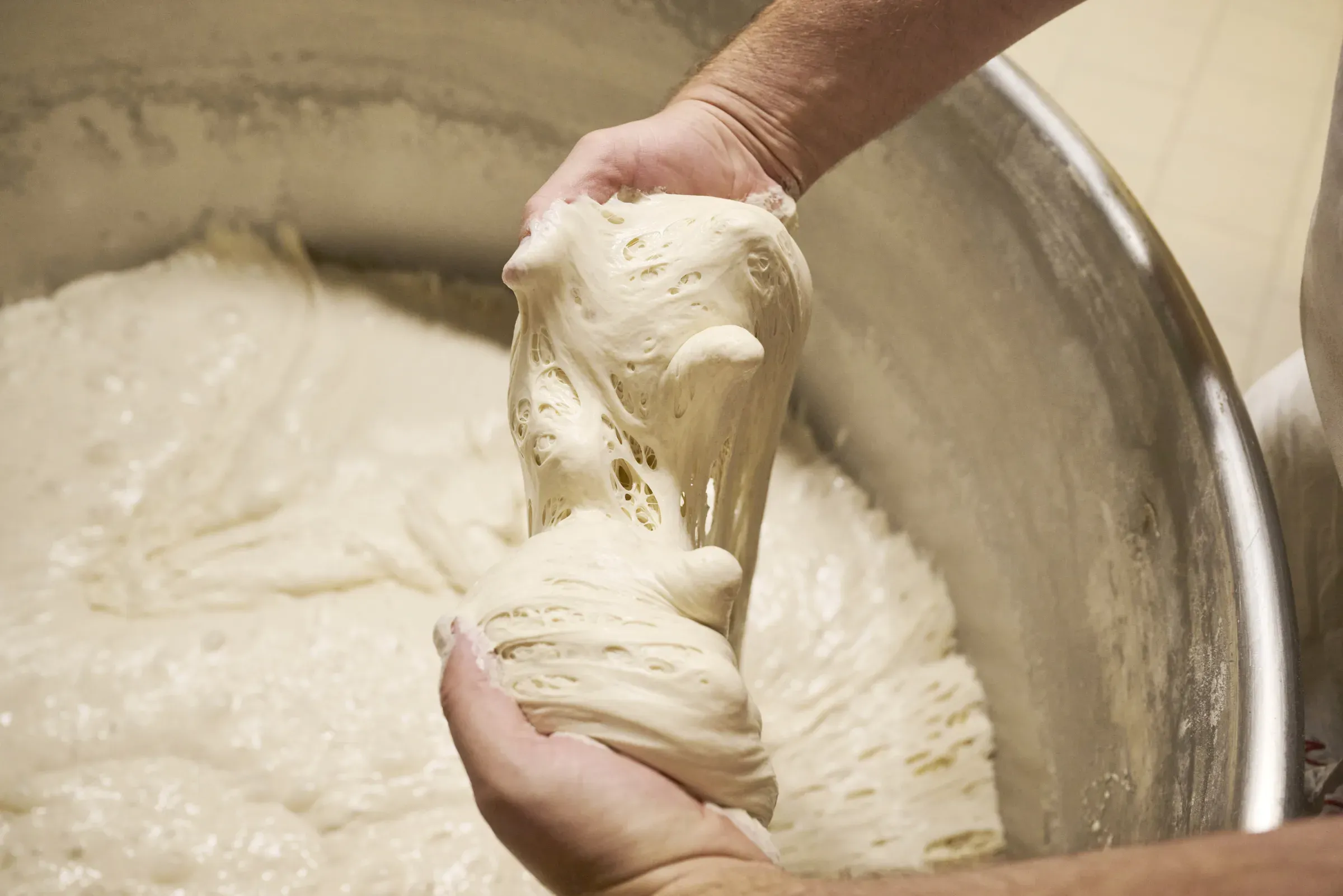Eine Hand hält eine Portion reifen Sauerteig über dem Kessel