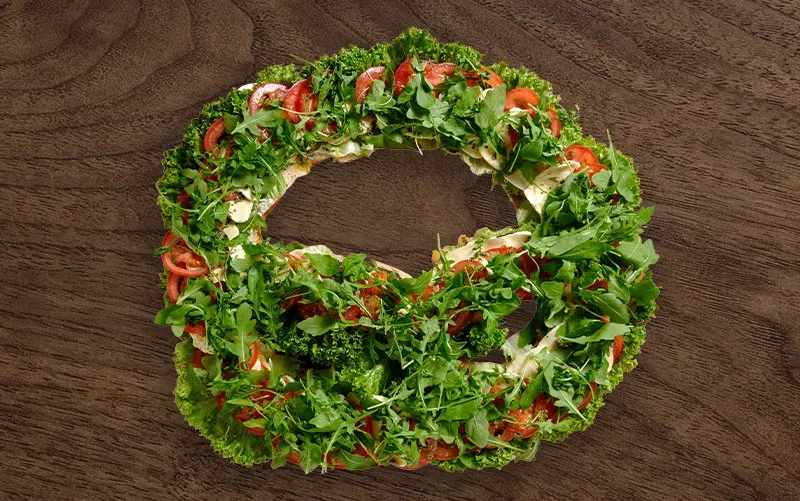Riesen-Brezel von oben, offen: die ganze Fläche ist mit Rucola, Tomatenscheiben und Mozzarella belegt.