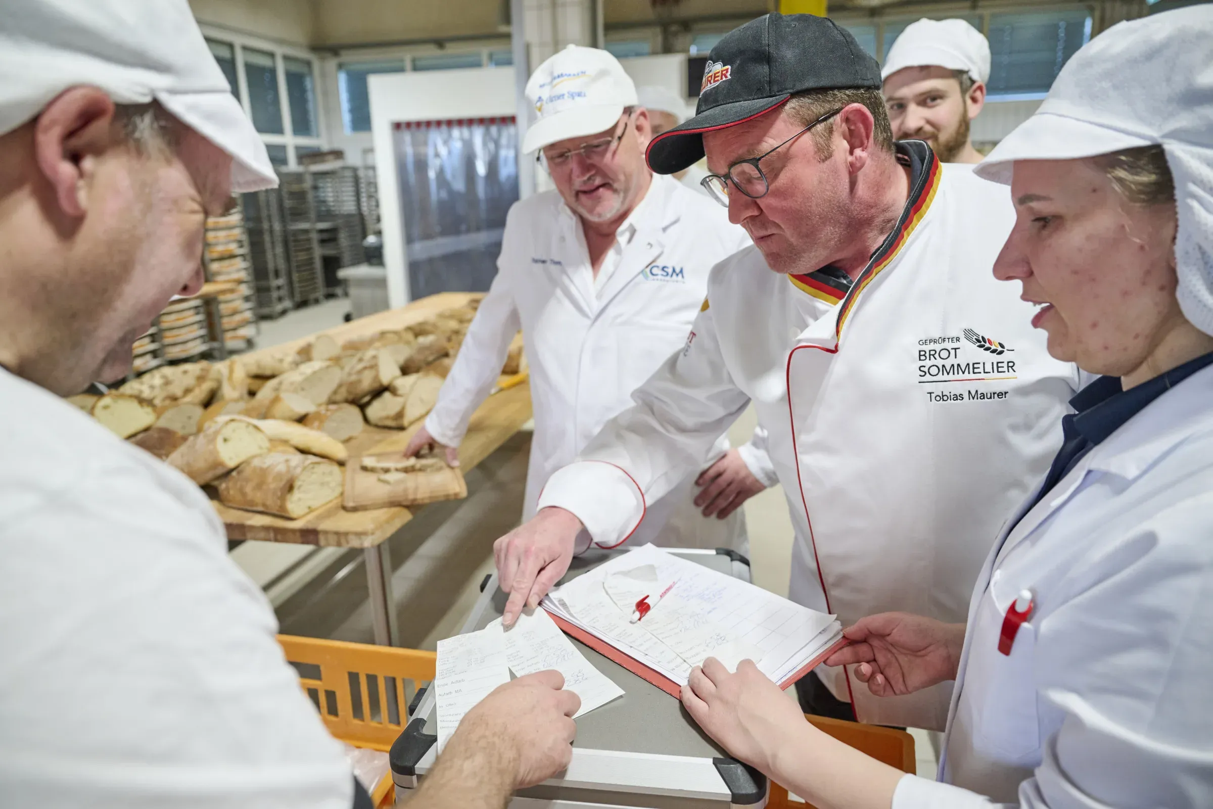 Drei Mitarbeitende tragen bei der Brotprüfung ihre Bewertung in einen Ordner ein