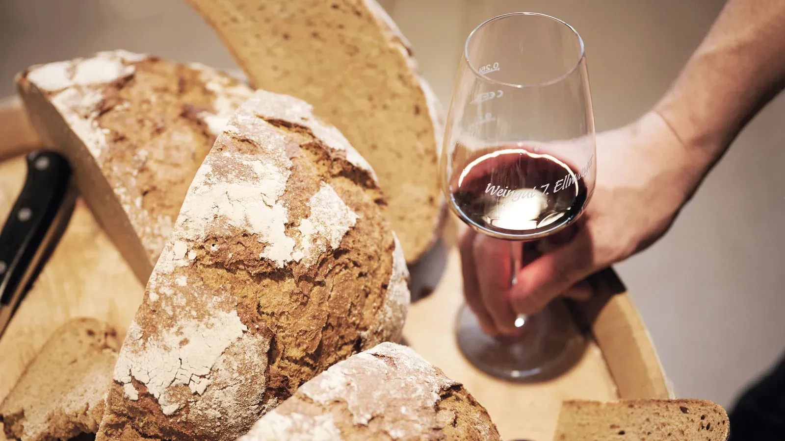 Hand hält ein Rotweinglas, nebenan liegt Brot